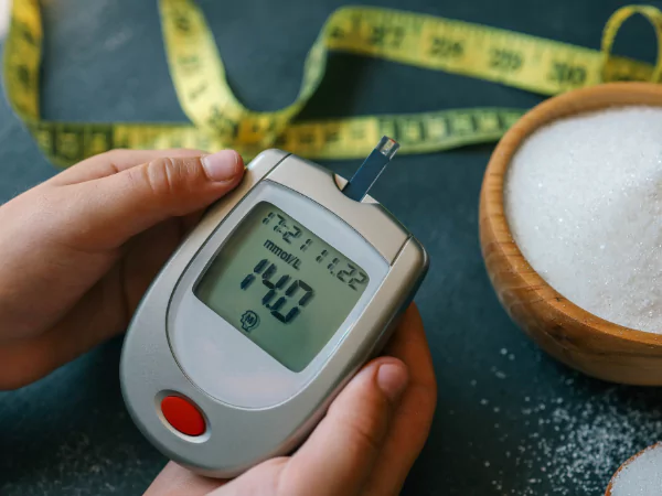 Cinta de medición, frasco de azúcar y mano con muestra de sangre, simbolizando el control de la diabetes