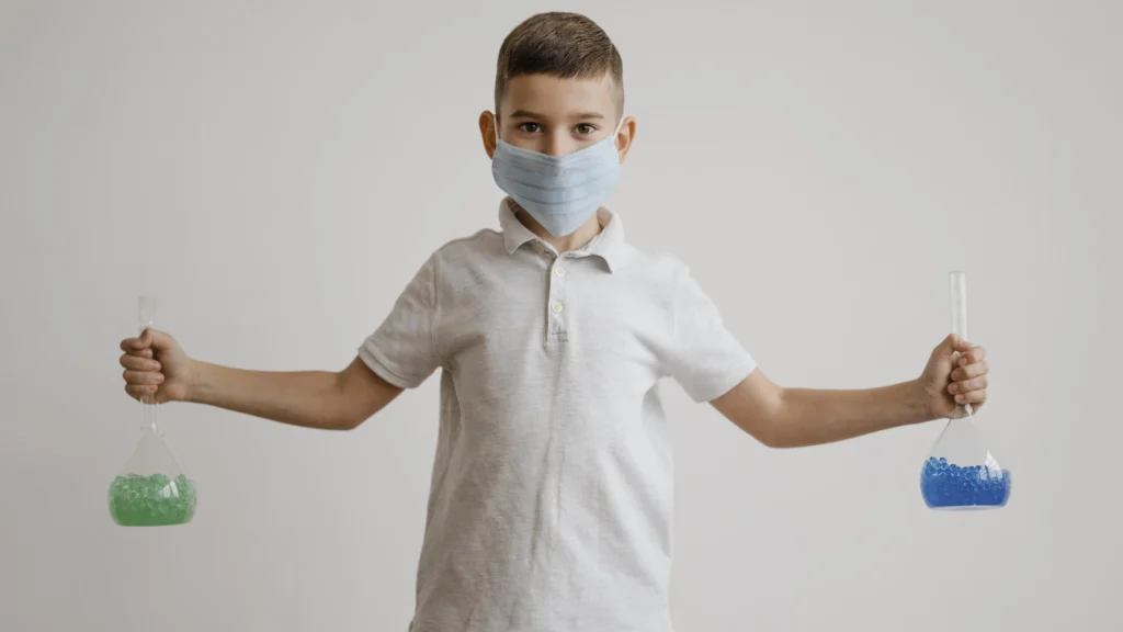 Niños con cubre bocas y fondo azul sostiene dos elementos en sus manos.