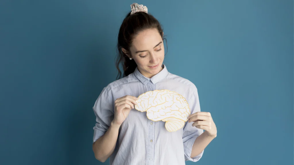 Mujer con fondo azul sostiene un cerebro amarillo.